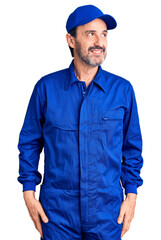 Middle age handsome man wearing mechanic uniform smiling looking to the side and staring away thinking.