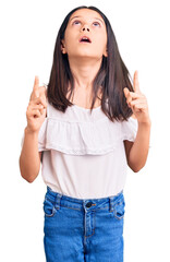 Beautiful child girl wearing casual clothes amazed and surprised looking up and pointing with fingers and raised arms.