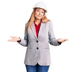 Beautiful young woman wearing architect hardhat clueless and confused expression with arms and hands raised. doubt concept.