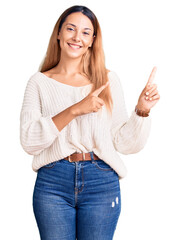 Beautiful young woman wearing casual clothes smiling and looking at the camera pointing with two hands and fingers to the side.