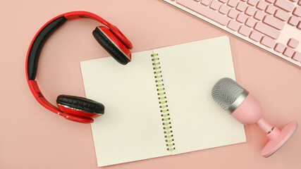 Above view of podcast recording equipment with headphone, microphone and notepad on pink background