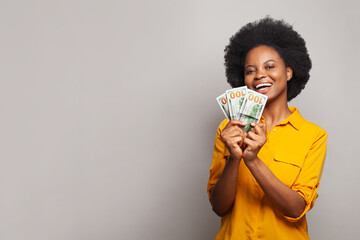 Happy young woman holding hundreds of dollar money banknotes and celebrating success on grey background. Finance, currency and people concept