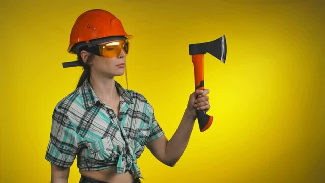 A Female builder in an orange safety helmet holds an ax in her hands