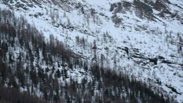 A rescue helicopter is flying in the Swiss Snowy alps during the winter to transport an injured skier to the hospital