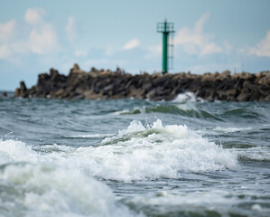 A storm in the Baltic Sea. Rough sea in the background a concrete breakwater with a lighthouse. Waves in the Baltic Sea, foamy water.