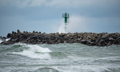 A storm in the Baltic Sea. Rough sea in the background a concrete breakwater with a lighthouse. Waves in the Baltic Sea, foamy water.