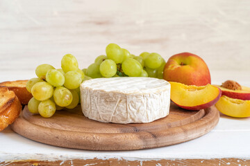 Camembert cheese, white grapes, fresh peach, wheat bread on wooden background.