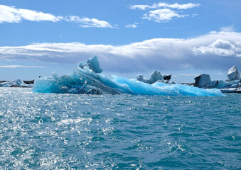A huge piece of translucent blue and turquoise ice is a beautiful iceberg that broke away from  glacier in the ocean off the coast of Iceland and melts