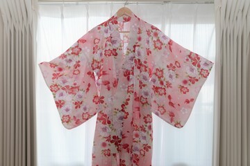 Japanese yukata with pink floral print hanging on a curtains