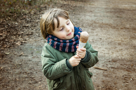 Toddler boy wearing warm jacket and scarf eating chocolate ice cream in waffle  cone with pleasue,  outdoor in cold weather.