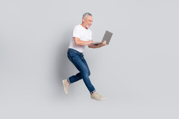 Full length body size view of handsome cheerful man jumping using laptop typing email isolated over grey pastel color background