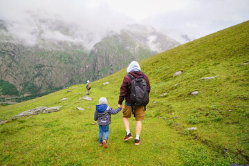 Father and sons hiking together, view from the back, long walk, summer activities for family in the mountains.