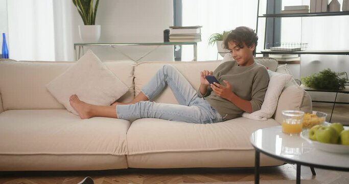 Happy teenager sits playing interesting games on smartphone