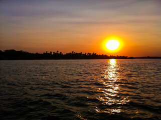 Sonnenuntergang über Meeresspiegel. Dunkle Silhouette einer Insel am Horizont. Orangenes Sonnenlicht, blau roter Himmel. Licht im Wasser gespiegelt.