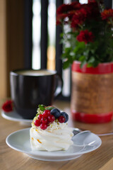 The soft curves of a Pavlova dessert garnished with colorful fruits, presenting a delightful contrast to the rustic cafe ambiance
