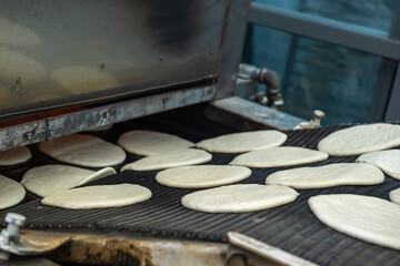 Pita bread making process. Automated belt loading pita bread into the oven.