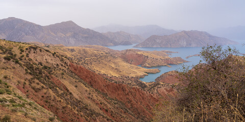 Panoramic landscape view of colorful Nurek or Norak dam lake and valley between Dushanbe and Khatlon regions in Tajikistan on overcast summer day - obrazy, fototapety, plakaty