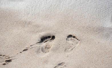 Fototapeta na wymiar Traces of children's feet in the wet sand at the beach. Sandy beach with footprints. Beach holiday.