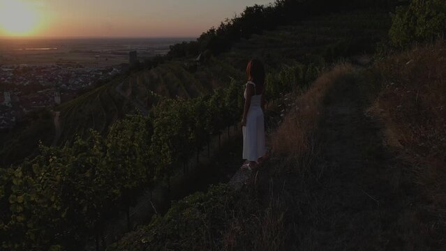Young woman in white dress seeing the sun set over the vineyard countryside 
