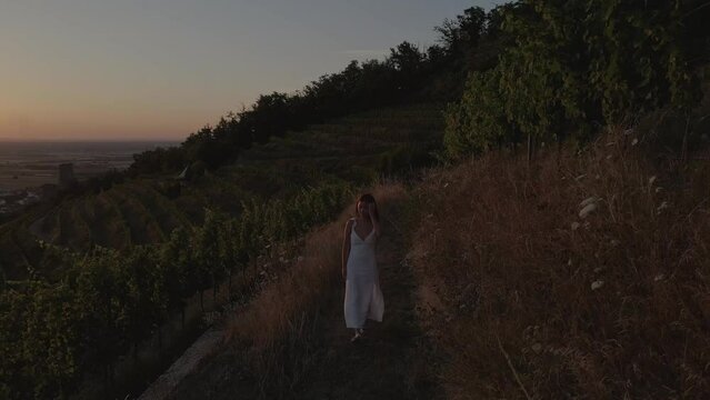 Front view Young woman with white dress walking around a grass meadow at sunset in the Schriesheim region with vineyard surroundings