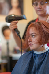 A brown-haired girl is sitting in a chair at the hairdresser doing her hair and styling her hair.