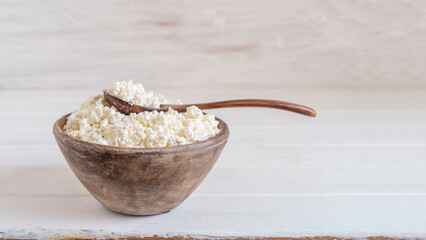 Cottage cheese in wooden bowl over white background with copy space.