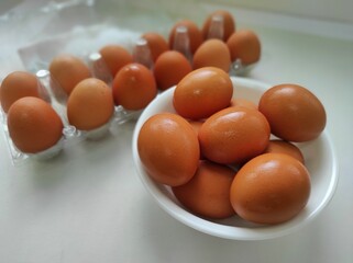 Brown chicken eggs in plastic container and white bowl on white background.