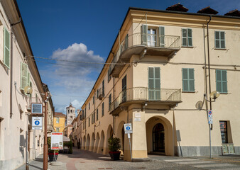 Fototapeta na wymiar Fossano, Cuneo, Italy - August 25, 2022: the historic center with via Cavour, pedestrian street with arcades and the civic bell tower at the bottom, blue sky with clouds