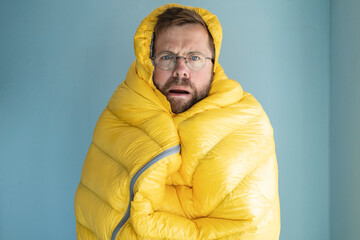Alarmed man froze and wrapped himself in a warm sleeping bag, standing indoors against the...