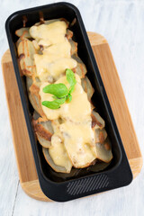 Potato casserole in shape on a wooden board on a light table.