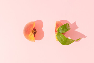Fresh juicy peach with pit and leaves cut in half on pastel pink background. Minimal fruit concept. Healthy raw food trendy composition. Summer party aesthetic. Flat lay.