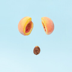 Peach pit dropping from two cut halves of fresh peach against pastel blue background. Creative fruit concept. Minimal healthy food composition.