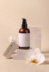 Dark glass cosmetic bottle with blank label near white orchid flowers and stones, Mockup