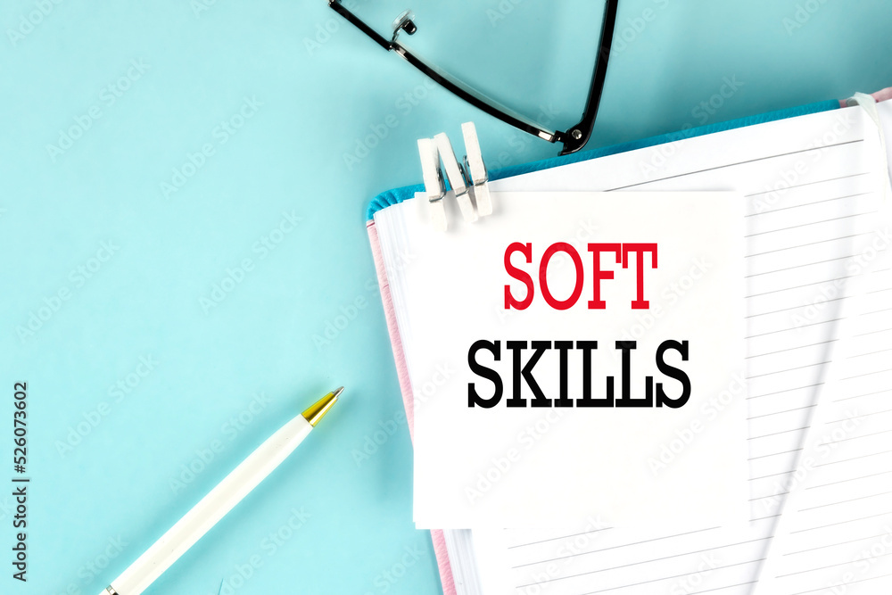 Poster soft skills text on a sticky on notebook with pen and glasses , blue background