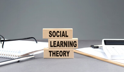 SOCIAL LEARNING THEORY text on wooden block with notebook,chart and calculator, grey background