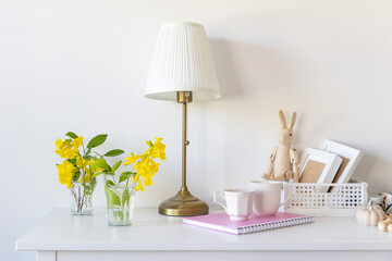 White floor lamp with lampshade. A pink notebook with springs, a white coffee mug, a wooden toy...