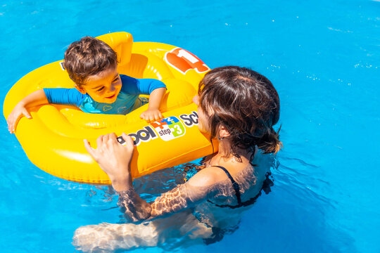 Mother Playing With Her Son With A Yellow Float In The Pool In Summer