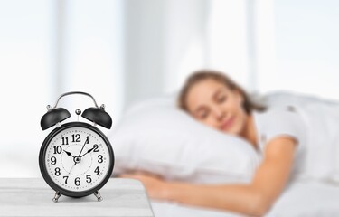 Classic alarm clock on bedside table in bedroom, with happy peaceful young woman sleeping on bed....