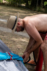 Hombre en bañador y gorro en el camping, montando tienda de campaña. Vacaciones de verano.
