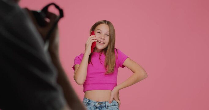 Funny busy child girl star model actress answering call during photo shooting in studio, posing for photos