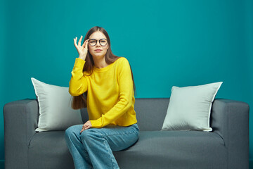 Young girl student fixes glasses, looking at camera, squinting, straining eyes, sitting on sofa....