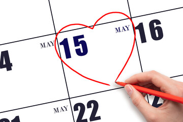 A woman's hand drawing a red heart shape on the calendar date of 15 May. Heart as a symbol of love.