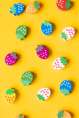 Colored wooden figures in the form of strawberries on a yellow background