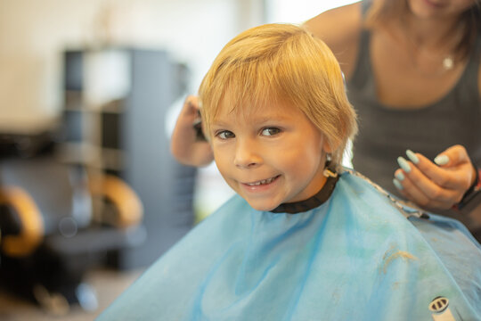 Cute toddler blond boy, having haircut in hairdresser salloon