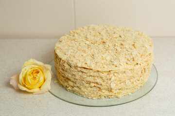 Homemade Napoleon cake stands on the table with a yellow rose next to it