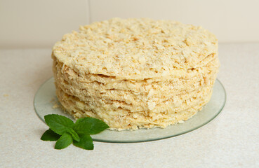 Homemade Napoleon Cake stands on the table in the kitchen. It is decorated with a sprig of mint