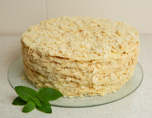 Homemade Napoleon Cake stands on the table in the kitchen. It is decorated with a sprig of mint