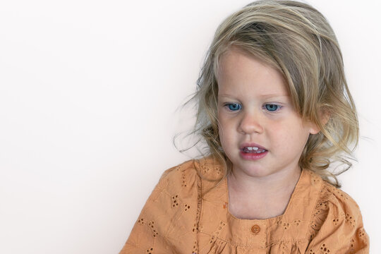Pensive white caucasian girl 2 years old with beautiful blue eyes with blond hair in her hands in a brown dress with copy space