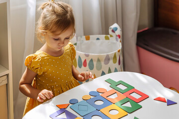 A little girl playing with wooden shape sorter toy on the table in playroom. Educational boards for Color and Shapes sorting for toddler. Learning through play. Developing Montessori activities.