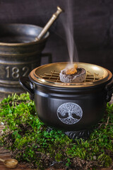 Aromatic frankincense resins on glowing charcoal in a witch cauldron with symbol 